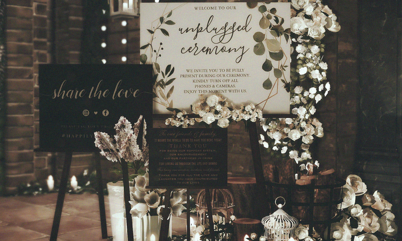 Ein dunkles Bild mit vielen Hochzeits-CC-Schildern, auf denen "unplugged ceremony" oder "share the love" steht. Sie sind von Laternen und Blumen umgeben.